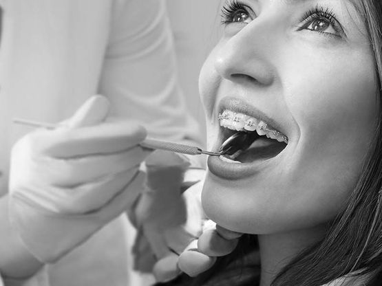 Kieferorthopäde untersucht mit Zahnarztspiegel die Brackets einer Patientin