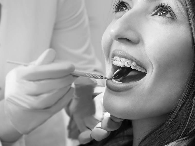 Kieferorthopäde untersucht mit Zahnarztspiegel die Brackets einer Patientin